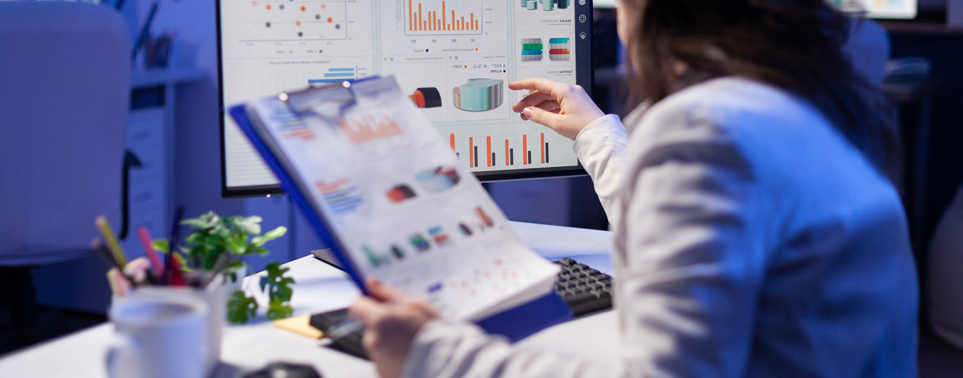 scientist in lab coat in front of computer holding a clipboard