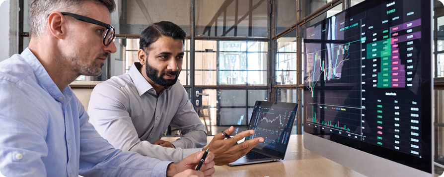 Two males at a desk sitting in front of a laptop and monitor wall