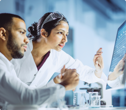 female and male in lab coats looking at a monitor